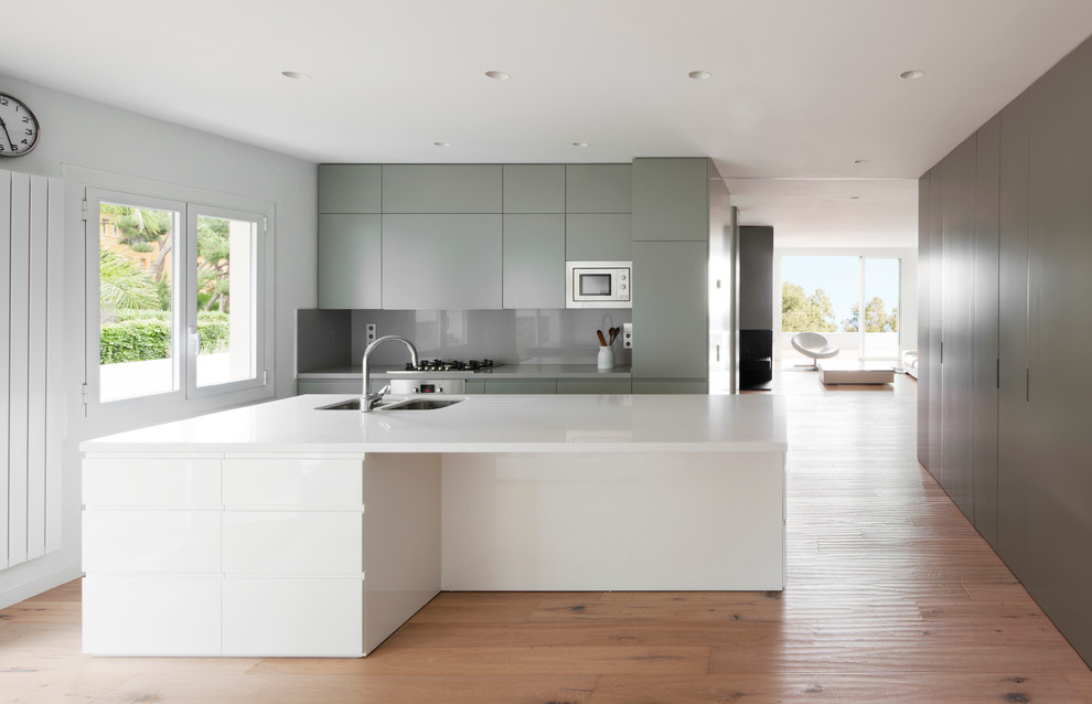This is an example of a mid-sized modern galley separate kitchen in Other with flat-panel cabinets, grey cabinets, with island, grey splashback, an undermount sink, solid surface benchtops and medium hardwood floors.