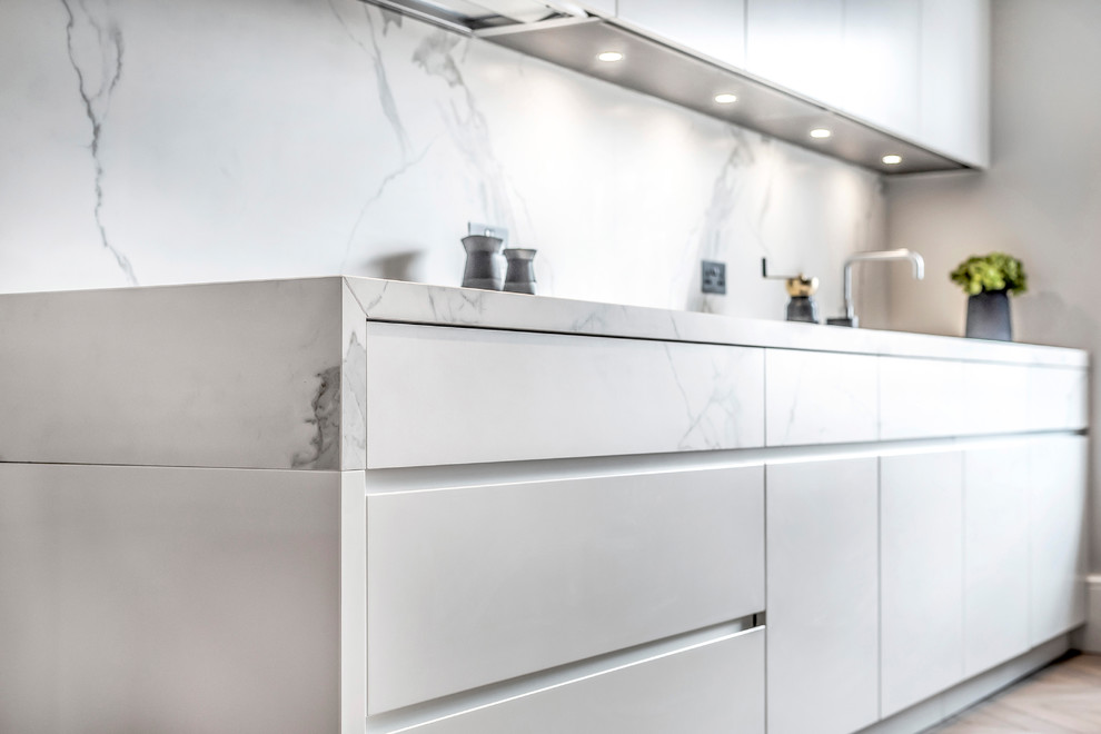 This is an example of a contemporary galley separate kitchen in London with grey cabinets, white splashback, marble splashback, medium hardwood floors, with island, brown floor, white benchtop and flat-panel cabinets.