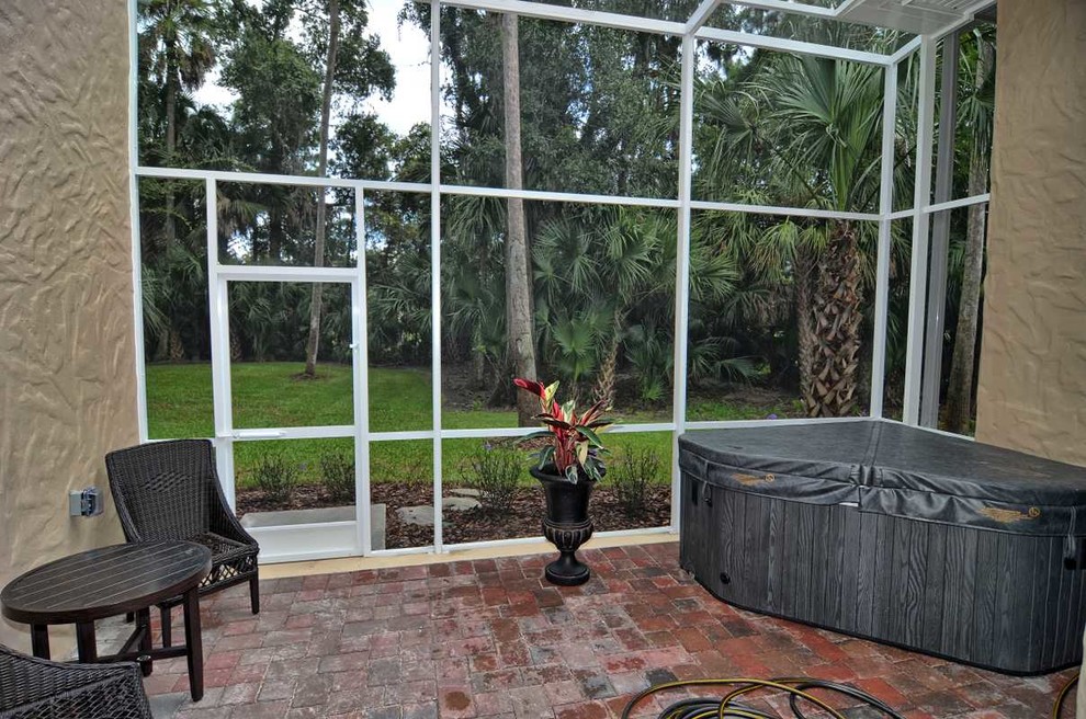 This is an example of a mid-sized traditional backyard screened-in verandah in Orlando with brick pavers and an awning.