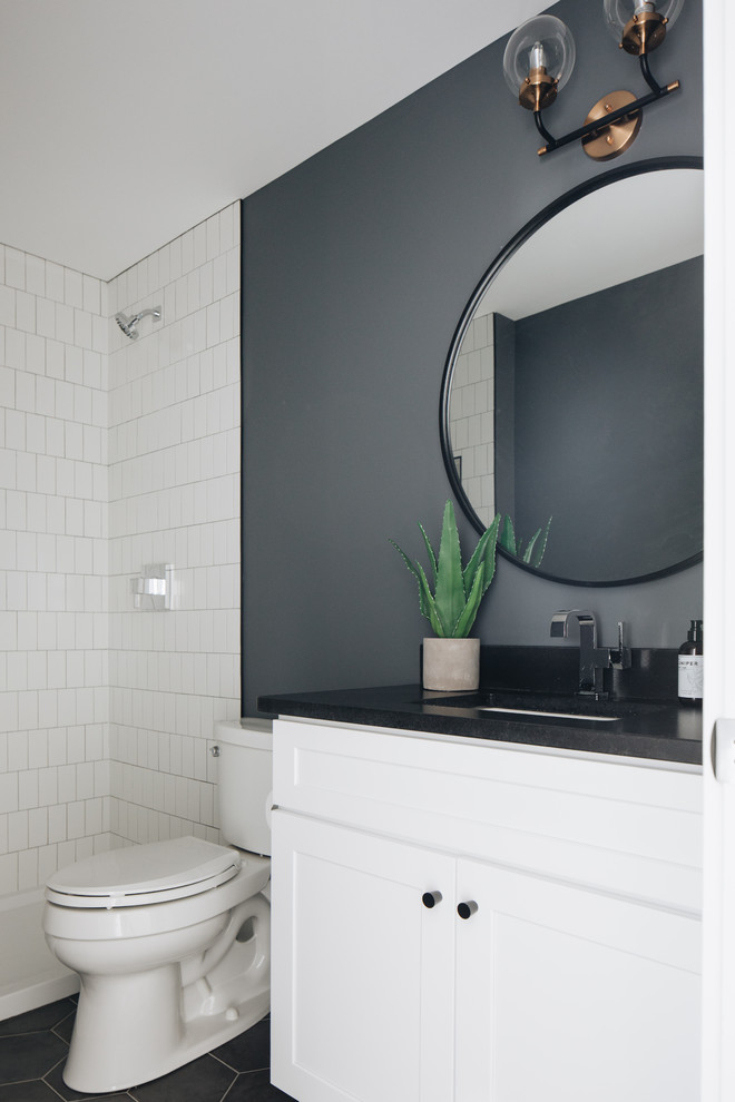 This is an example of a beach style 3/4 bathroom in Chicago with shaker cabinets, white cabinets, a two-piece toilet, white tile, grey walls, an undermount sink, grey floor and black benchtops.