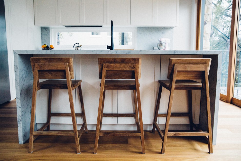 This is an example of a contemporary l-shaped open plan kitchen in Sydney with white cabinets, marble benchtops, grey splashback, stone slab splashback, stainless steel appliances, medium hardwood floors, with island, an undermount sink and recessed-panel cabinets.