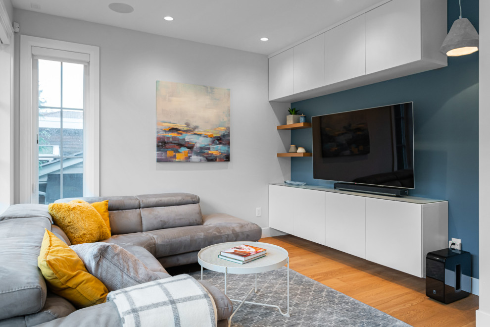 This is an example of a small contemporary open concept living room in Vancouver with a library, blue walls, light hardwood floors, a built-in media wall and brown floor.