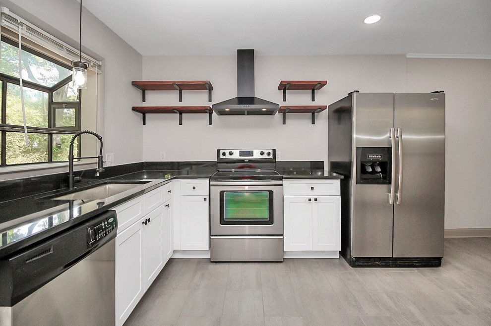 This is an example of a small industrial l-shaped eat-in kitchen in Charlotte with an undermount sink, shaker cabinets, white cabinets, granite benchtops, black splashback, granite splashback, stainless steel appliances, ceramic floors, no island, grey floor and black benchtop.