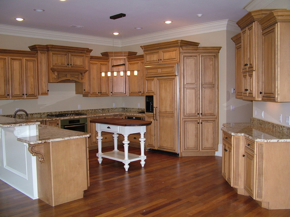 Open concept kitchen - mid-sized traditional u-shaped medium tone wood floor and brown floor open concept kitchen idea with raised-panel cabinets, light wood cabinets, granite countertops, paneled appliances, an island and beige countertops