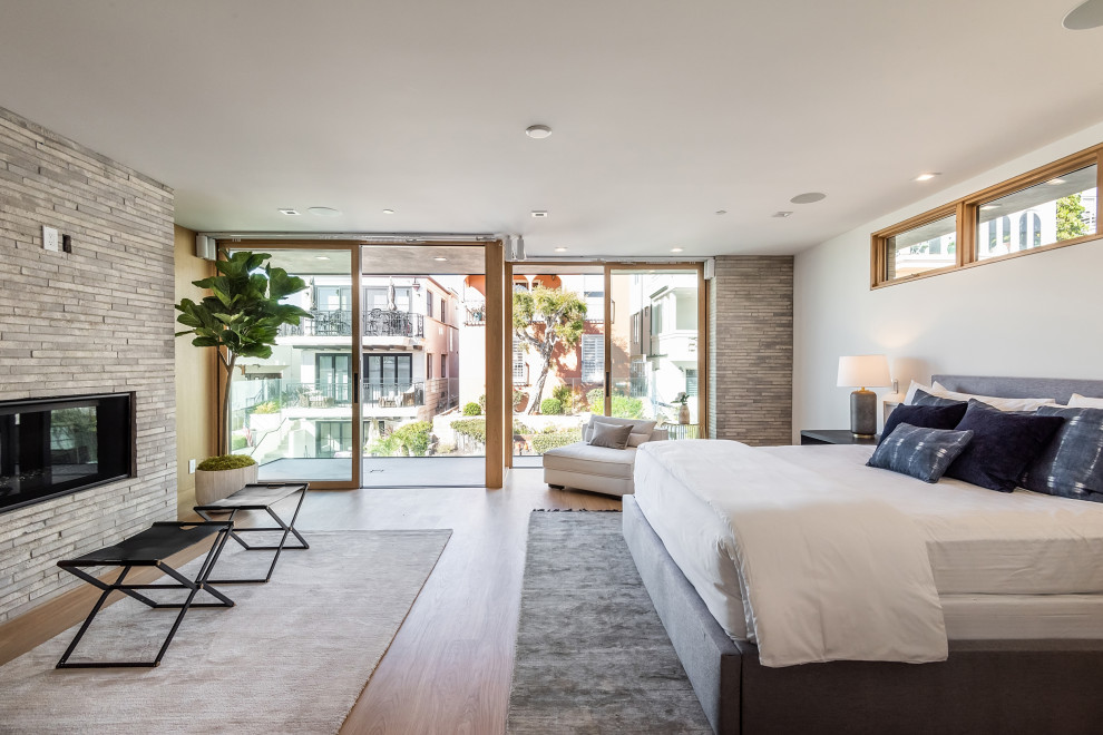 Large contemporary master bedroom in Los Angeles with white walls, a ribbon fireplace, a tile fireplace surround and brown floor.