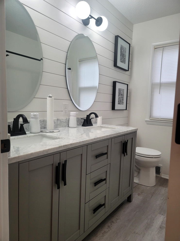 Lantlig inredning av ett litet vit vitt en-suite badrum, med skåp i shakerstil, grå skåp, ett badkar i en alkov, en toalettstol med separat cisternkåpa, vita väggar, vinylgolv, ett undermonterad handfat, marmorbänkskiva och grått golv
