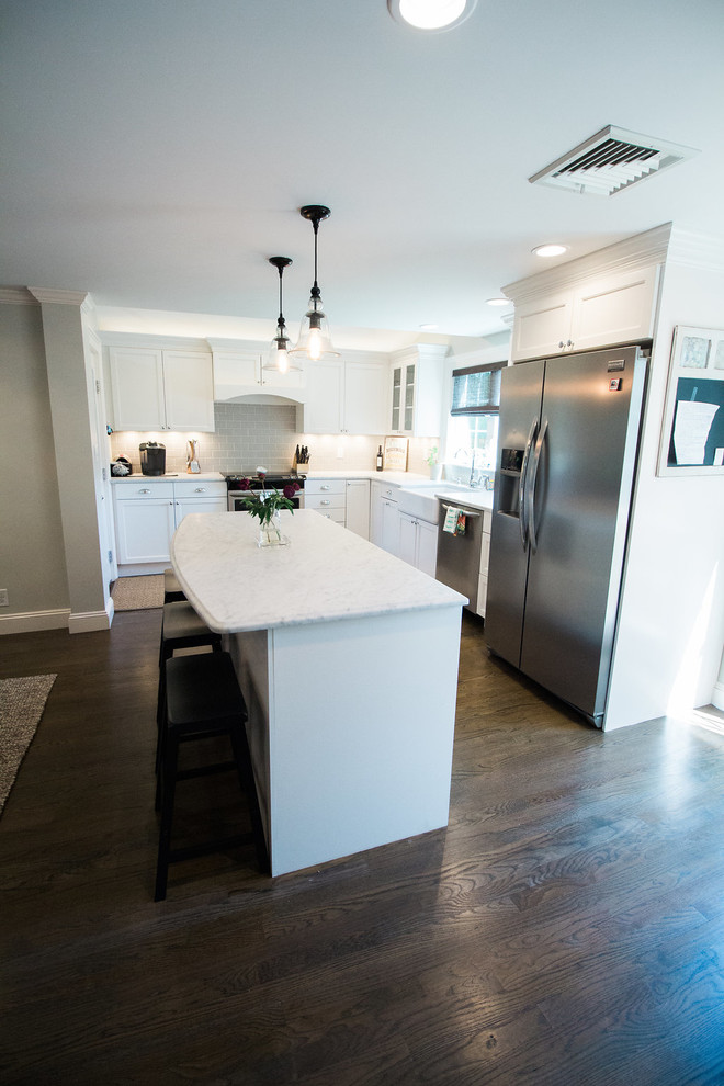 Mid-sized transitional l-shaped dark wood floor and brown floor eat-in kitchen photo in Boston with a farmhouse sink, shaker cabinets, white cabinets, marble countertops, gray backsplash, subway tile backsplash, stainless steel appliances and an island