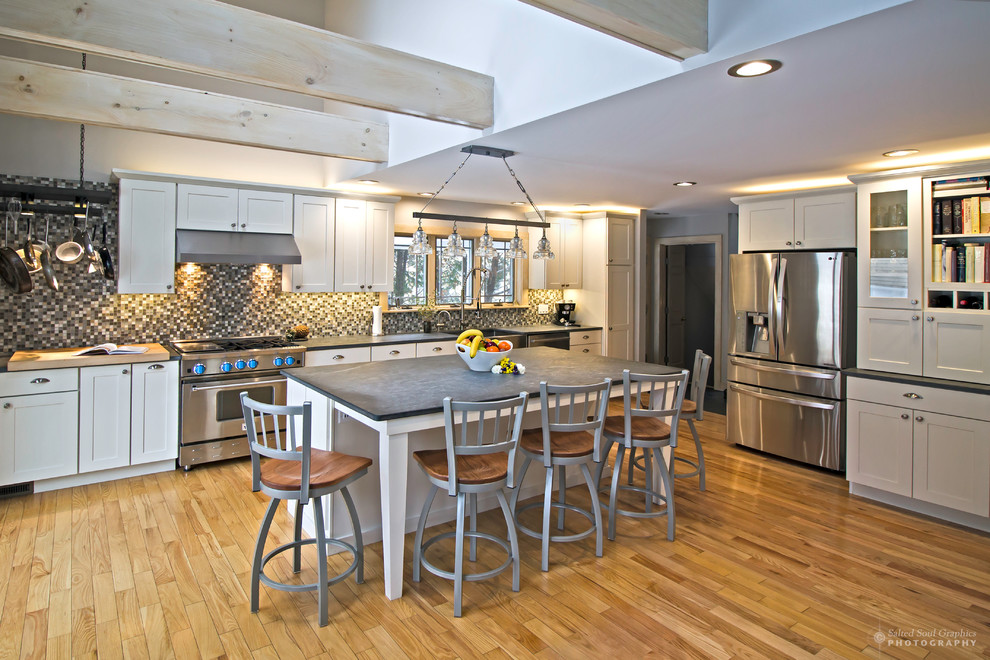 Large mountain style l-shaped light wood floor open concept kitchen photo in Burlington with an undermount sink, shaker cabinets, white cabinets, soapstone countertops, multicolored backsplash, glass tile backsplash, stainless steel appliances and an island