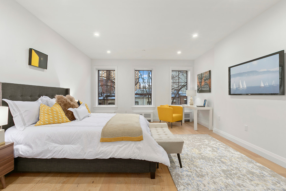 This is an example of a large contemporary master bedroom in New York with grey walls, light hardwood floors, no fireplace and brown floor.
