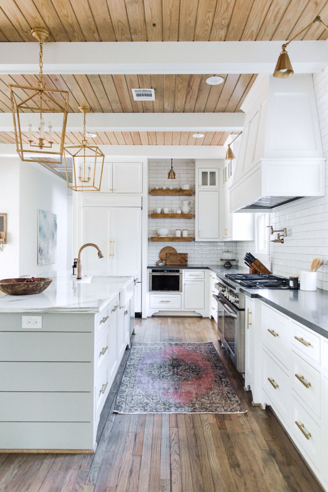 Country l-shaped kitchen in Houston with a farmhouse sink, shaker cabinets, white cabinets, white splashback, subway tile splashback, medium hardwood floors, with island, brown floor and grey benchtop.