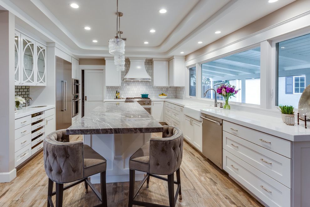 Photo of a large transitional u-shaped separate kitchen in Sacramento with a farmhouse sink, shaker cabinets, white cabinets, quartzite benchtops, grey splashback, marble splashback, stainless steel appliances, with island, brown floor, white benchtop and porcelain floors.