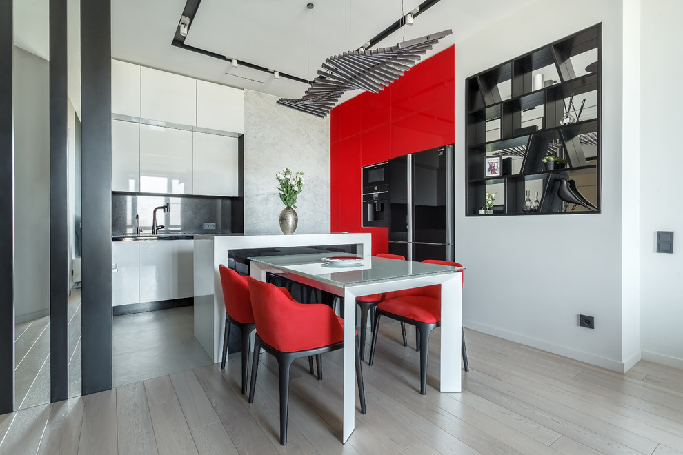 Photo of a contemporary l-shaped eat-in kitchen in Moscow with flat-panel cabinets, red cabinets, black splashback, black appliances, light hardwood floors, with island, beige floor and white benchtop.