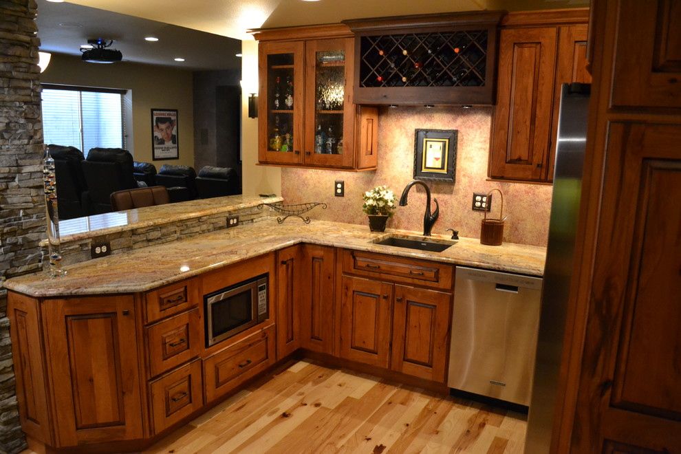 Design ideas for a mid-sized country open plan kitchen in Denver with an undermount sink, raised-panel cabinets, medium wood cabinets, granite benchtops, black splashback, stainless steel appliances and light hardwood floors.