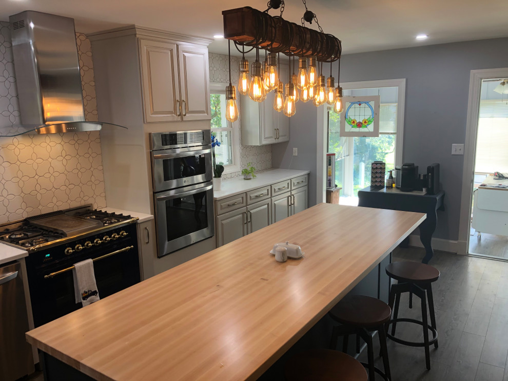 Kitchen - mid-sized transitional l-shaped vinyl floor and brown floor kitchen idea in DC Metro with a farmhouse sink, raised-panel cabinets, gray cabinets, solid surface countertops, white backsplash, ceramic backsplash, stainless steel appliances, an island and white countertops