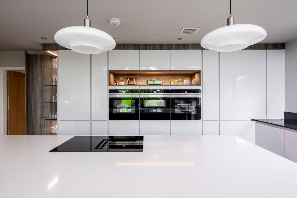 Foto på ett stort funkis vit kök, med en dubbel diskho, släta luckor, vita skåp, bänkskiva i kvartsit, grått stänkskydd, integrerade vitvaror och en köksö