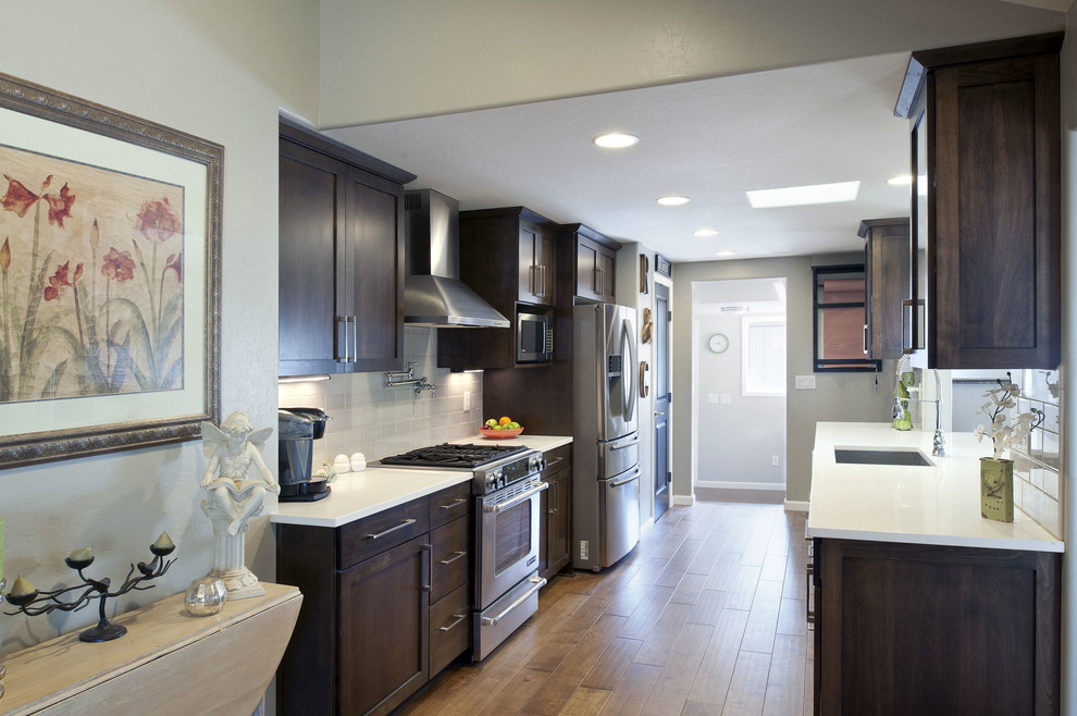 Example of a mid-sized transitional galley light wood floor and brown floor eat-in kitchen design in Phoenix with an undermount sink, shaker cabinets, dark wood cabinets, gray backsplash, glass tile backsplash, stainless steel appliances, no island and quartz countertops