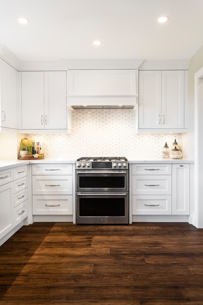 Large transitional u-shaped dark wood floor and brown floor eat-in kitchen photo in Toronto with an undermount sink, recessed-panel cabinets, white cabinets, quartz countertops, white backsplash, ceramic backsplash, stainless steel appliances, an island and white countertops