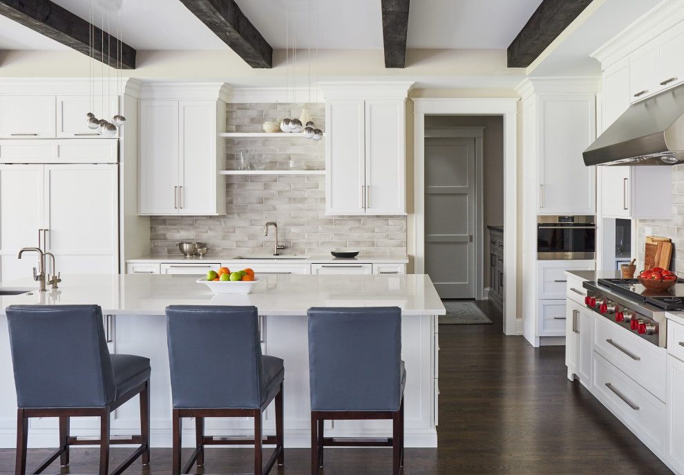 Design ideas for a large transitional l-shaped open plan kitchen in Chicago with an undermount sink, recessed-panel cabinets, white cabinets, quartz benchtops, grey splashback, porcelain splashback, panelled appliances, medium hardwood floors, with island, brown floor, white benchtop and exposed beam.