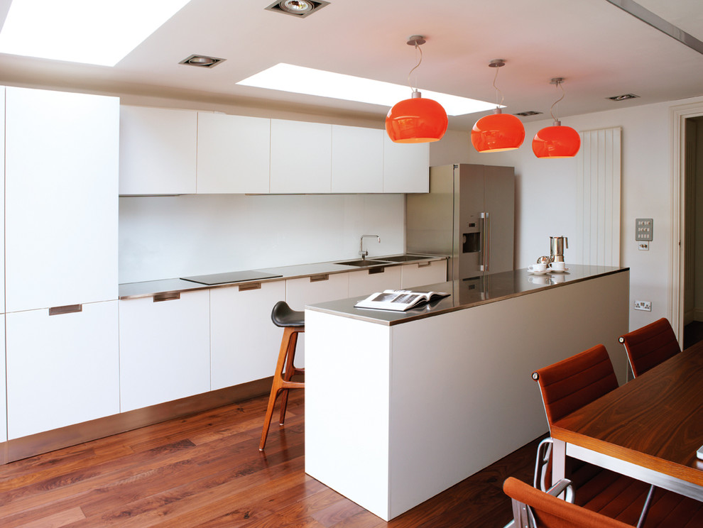 This is an example of a contemporary single-wall eat-in kitchen in London with a double-bowl sink, flat-panel cabinets, white cabinets, white splashback, stainless steel appliances, medium hardwood floors and with island.