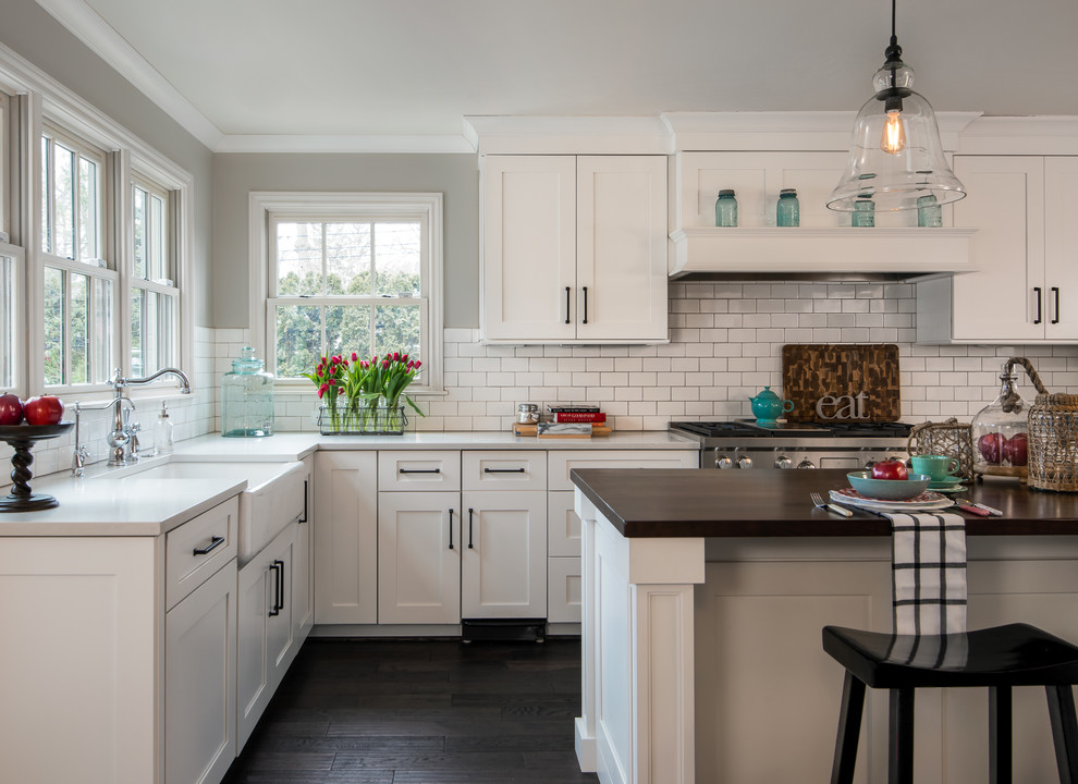 Inspiration for a large traditional l-shaped kitchen in Detroit with shaker cabinets, white cabinets, white splashback, subway tile splashback, stainless steel appliances, dark hardwood floors, with island, a farmhouse sink, quartz benchtops, brown floor and white benchtop.