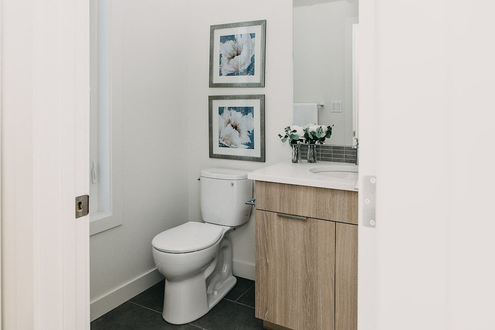 Mid-sized modern powder room in Edmonton with shaker cabinets, light wood cabinets, a one-piece toilet, white walls, an undermount sink, black floor and white benchtops.
