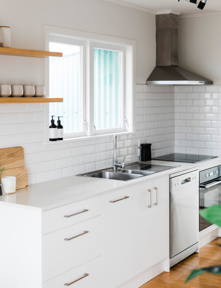 Design ideas for a mid-sized modern galley eat-in kitchen in Auckland with a double-bowl sink, white cabinets, quartz benchtops, white splashback, ceramic splashback, stainless steel appliances, light hardwood floors, brown floor and white benchtop.