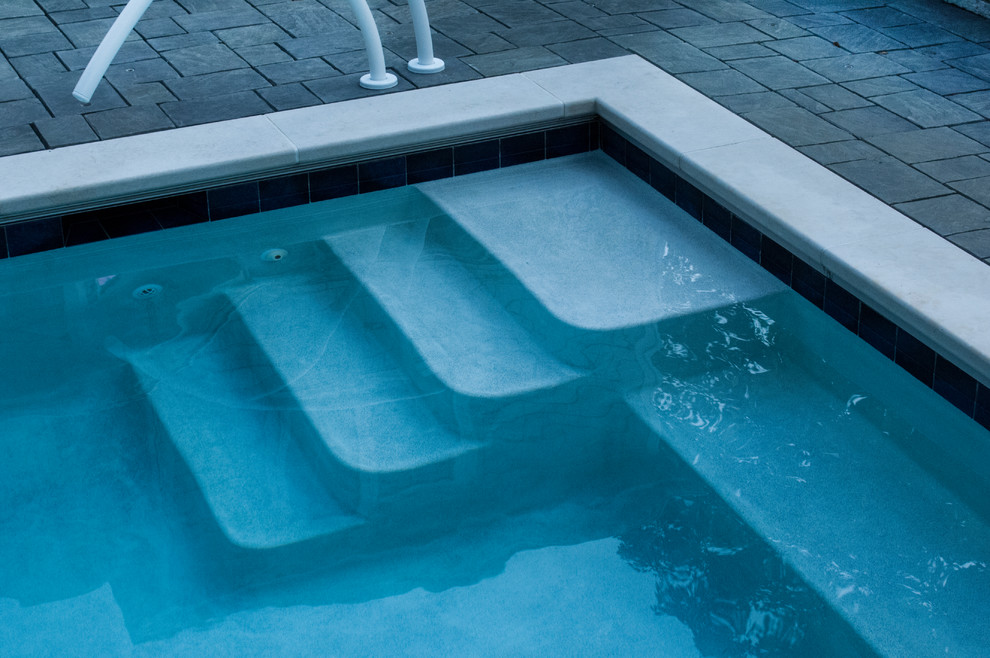 Ejemplo de piscina alargada tradicional pequeña rectangular en patio trasero con adoquines de hormigón