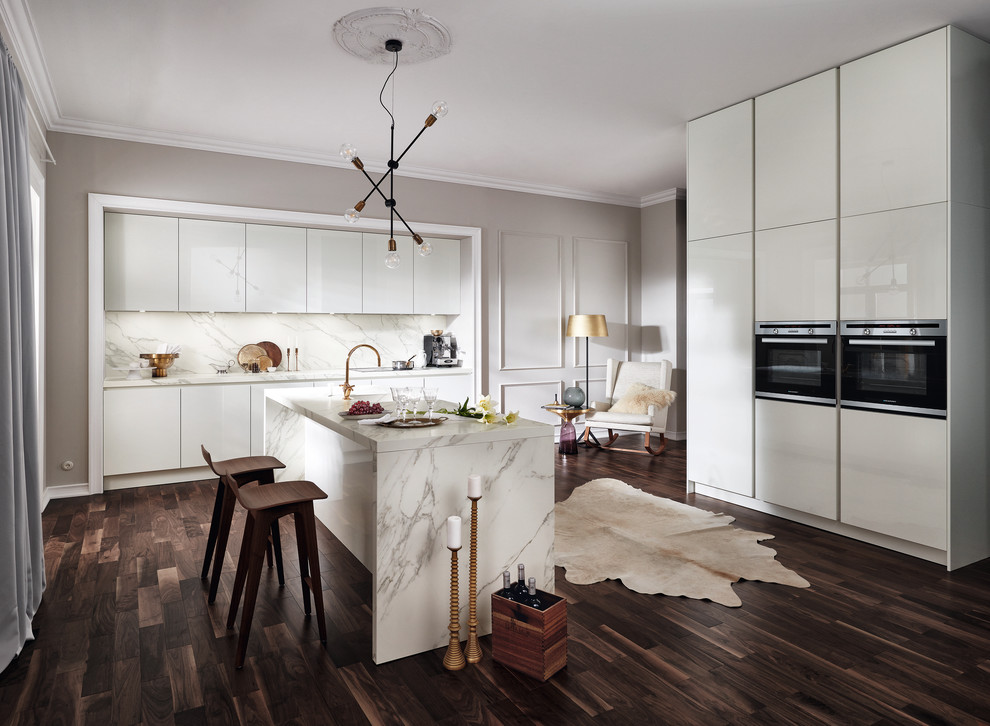 Inspiration for an expansive contemporary single-wall open plan kitchen in Dresden with an integrated sink, flat-panel cabinets, white cabinets, solid surface benchtops, white splashback, marble splashback, panelled appliances, dark hardwood floors, with island and brown floor.