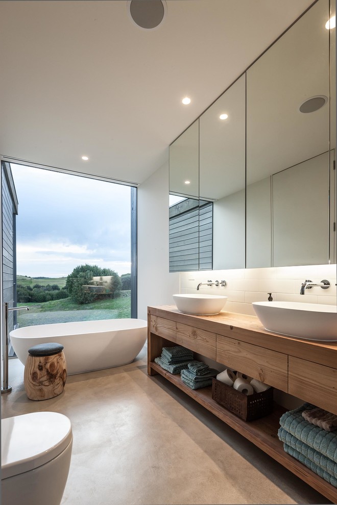 Photo of a contemporary bathroom in Melbourne with a vessel sink, flat-panel cabinets, light wood cabinets, wood benchtops, a freestanding tub, white tile and white walls.