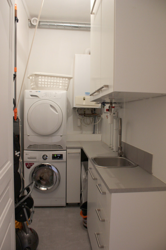 Photo of a small contemporary l-shaped laundry room in Other with an undermount sink, beaded inset cabinets, white cabinets, laminate benchtops, white walls, terra-cotta floors, a stacked washer and dryer, grey floor and grey benchtop.