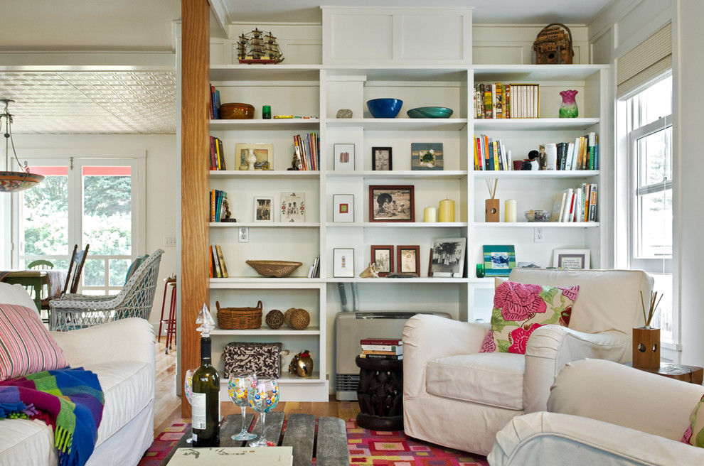 This is an example of a beach style living room in Portland Maine with a library and white walls.