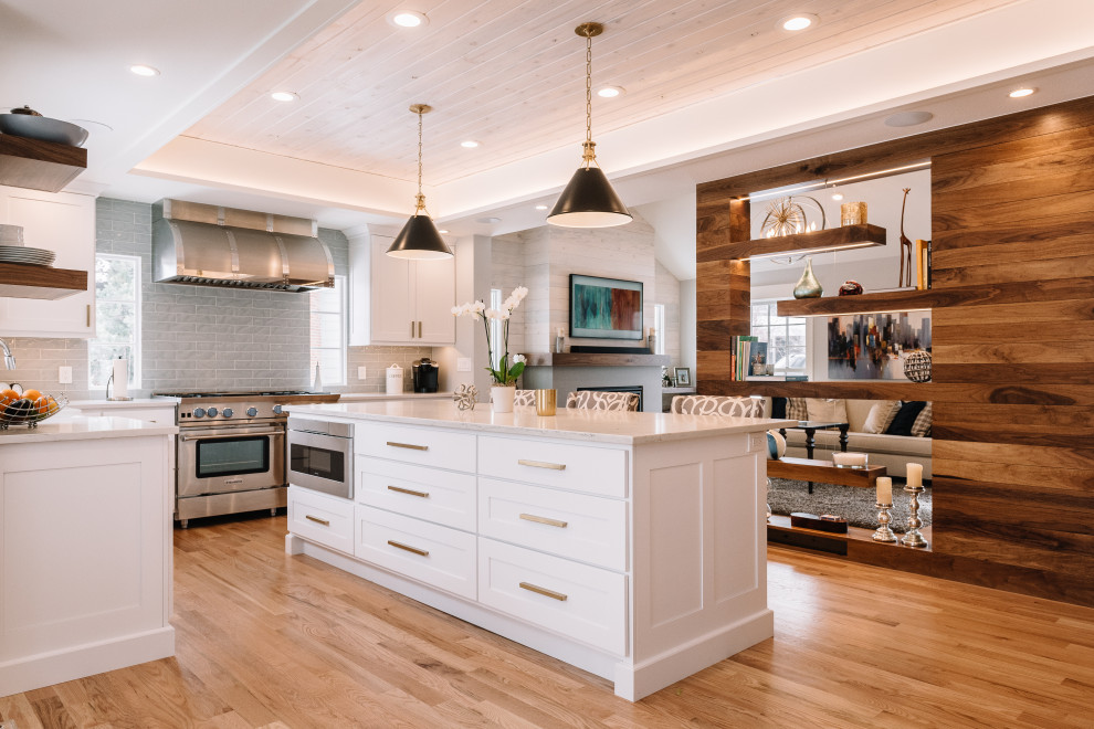 This is an example of a mid-sized l-shaped eat-in kitchen in Denver with a farmhouse sink, shaker cabinets, white cabinets, quartz benchtops, grey splashback, glass tile splashback, stainless steel appliances, light hardwood floors, with island, brown floor, white benchtop and recessed.