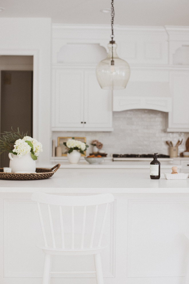 Foto på ett mellanstort vintage vit kök, med en nedsänkt diskho, skåp i shakerstil, vita skåp, bänkskiva i kvarts, vitt stänkskydd, stänkskydd i keramik, rostfria vitvaror, travertin golv, en köksö och brunt golv
