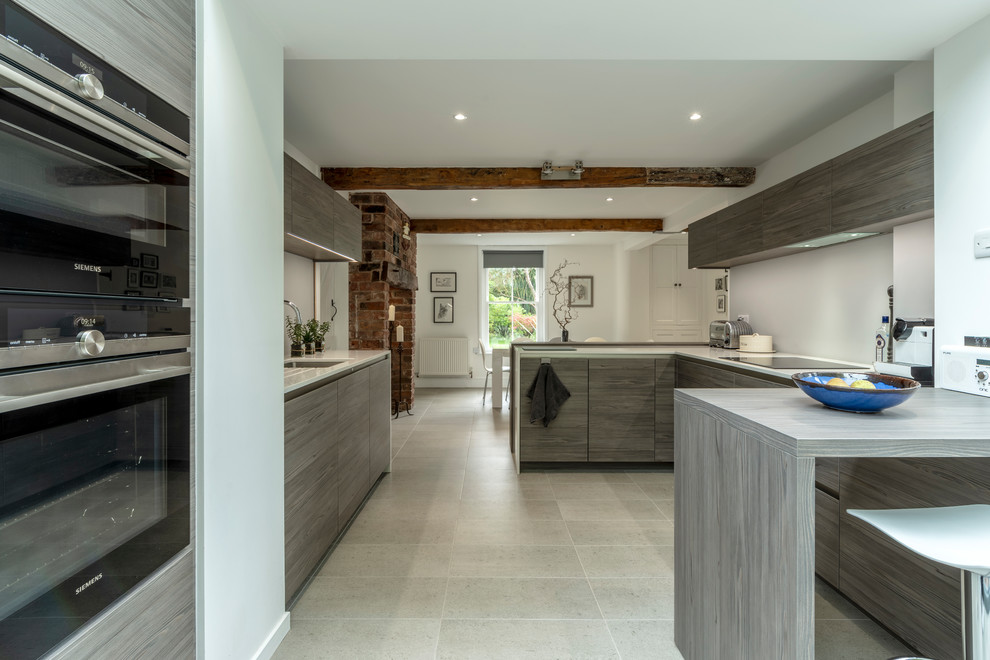Design ideas for a contemporary u-shaped eat-in kitchen in Cheshire with flat-panel cabinets, ceramic floors, beige floor, an undermount sink, grey cabinets, grey splashback, panelled appliances, a peninsula and white benchtop.