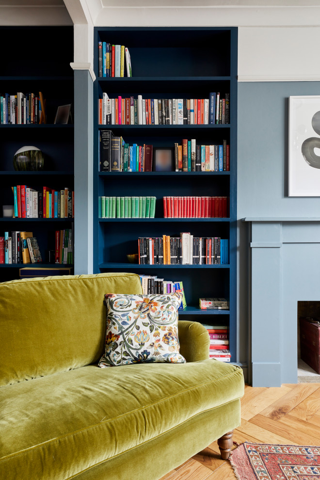 Photo of a small transitional enclosed living room in London with a library, blue walls, medium hardwood floors, a standard fireplace, a plaster fireplace surround and brown floor.