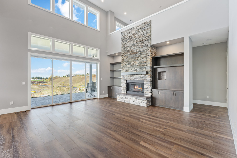 This is an example of an expansive classic open plan games room in Portland with grey walls, laminate floors, a standard fireplace, a stacked stone fireplace surround, brown floors and a vaulted ceiling.