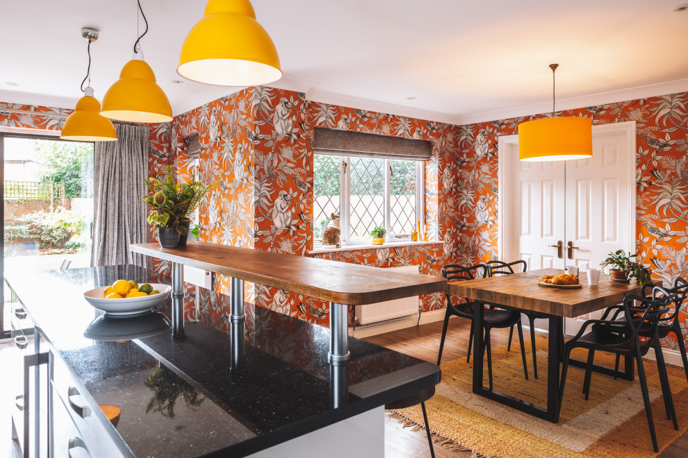 Design ideas for a mid-sized contemporary single-wall eat-in kitchen in Berkshire with an undermount sink, flat-panel cabinets, white cabinets, granite benchtops, orange splashback, cement tile splashback, coloured appliances, vinyl floors, with island, brown floor and black benchtop.