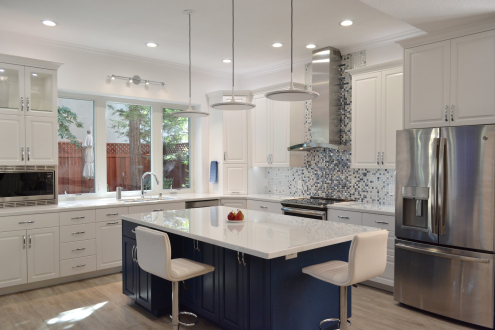 This is an example of a large transitional l-shaped open plan kitchen in San Francisco with a single-bowl sink, raised-panel cabinets, white cabinets, quartz benchtops, blue splashback, mosaic tile splashback, stainless steel appliances, laminate floors, with island, grey floor and white benchtop.