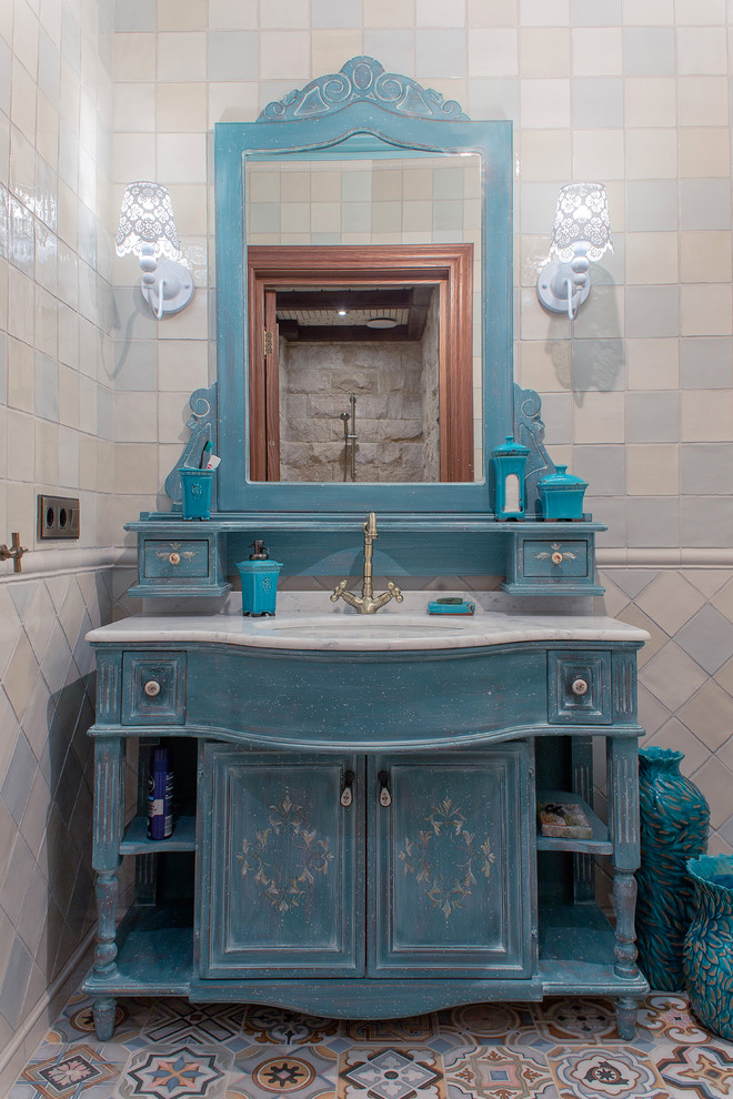 This is an example of a traditional powder room in Other with blue cabinets, multi-coloured tile, ceramic tile, ceramic floors, a vessel sink, marble benchtops, multi-coloured walls and furniture-like cabinets.