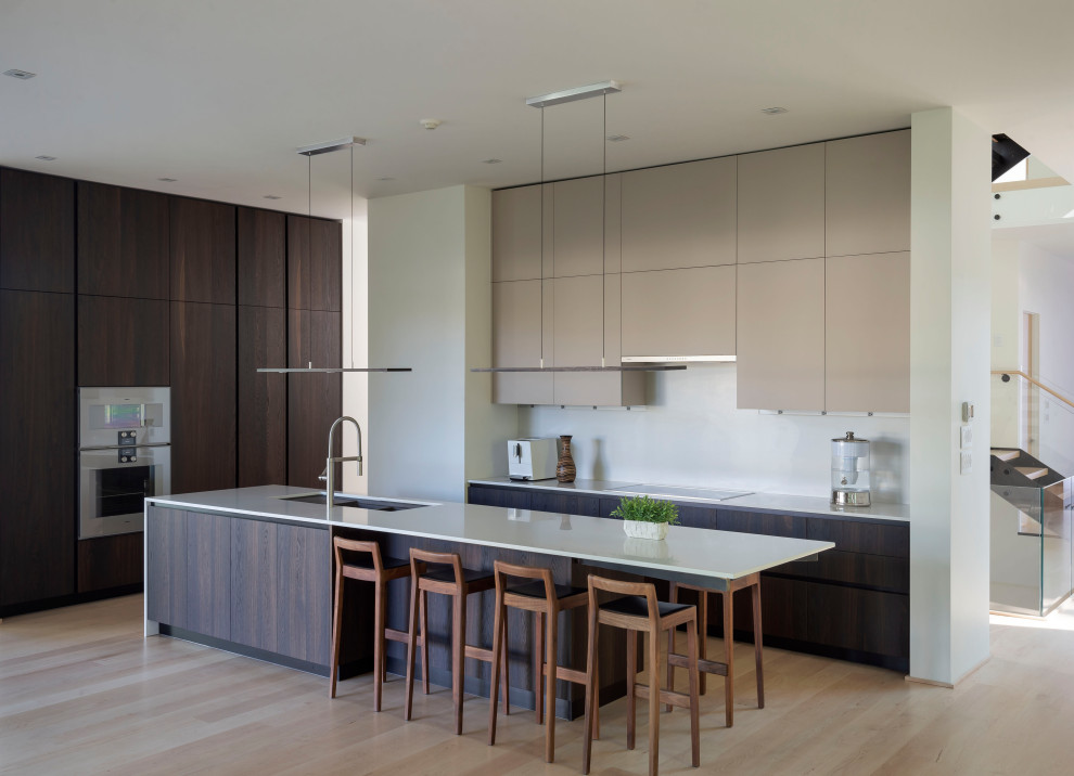 Inspiration for a large modern l-shaped kitchen in New York with a double-bowl sink, flat-panel cabinets, dark wood cabinets, panelled appliances, light hardwood floors, with island, beige floor and white benchtop.