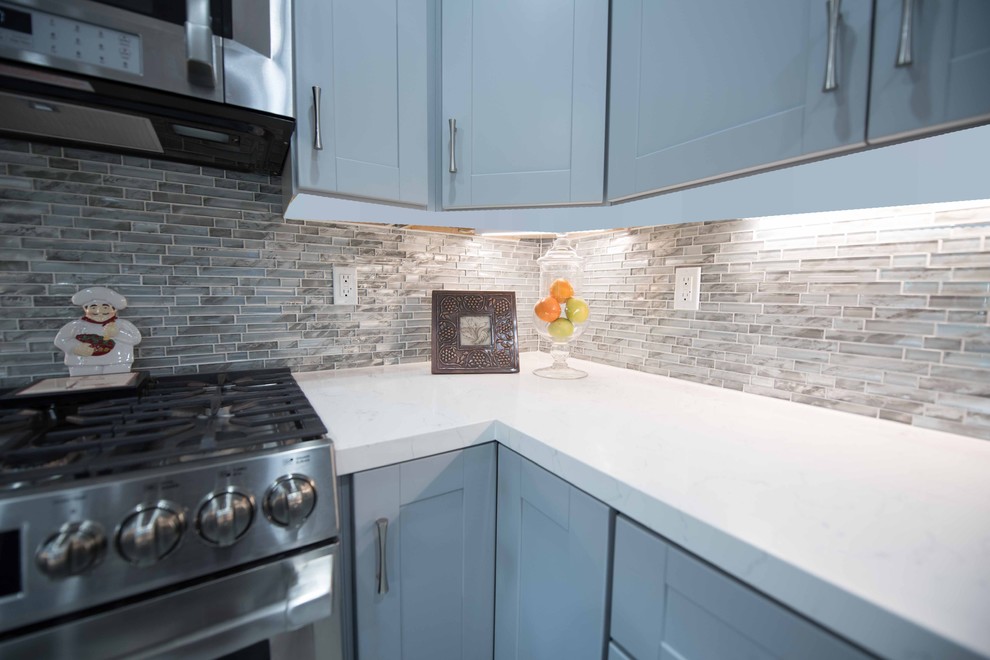 This is an example of a mid-sized transitional u-shaped separate kitchen in Los Angeles with a double-bowl sink, shaker cabinets, blue cabinets, quartz benchtops, beige splashback, glass tile splashback, stainless steel appliances, limestone floors and no island.