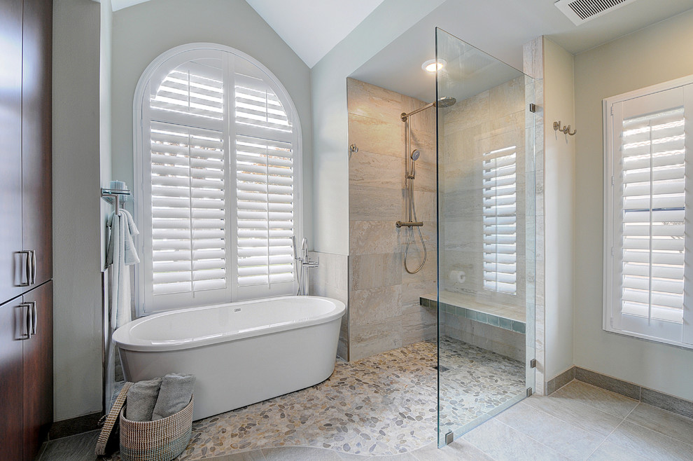 This is an example of a large beach style master bathroom in Tampa with an undermount sink, flat-panel cabinets, dark wood cabinets, granite benchtops, a freestanding tub, a curbless shower, a two-piece toilet, gray tile, porcelain tile, white walls and pebble tile floors.