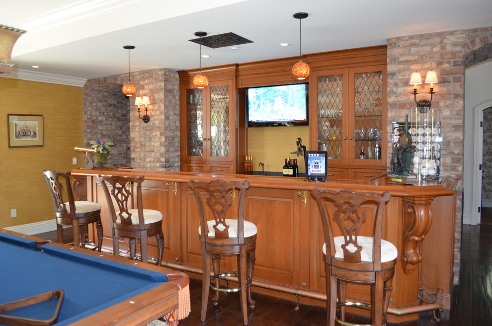This is an example of a large midcentury single-wall seated home bar in San Diego with dark hardwood floors, an undermount sink, glass-front cabinets, medium wood cabinets, wood benchtops, yellow splashback and brown floor.