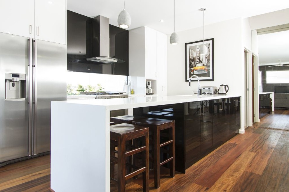 This is an example of a mid-sized modern galley eat-in kitchen in Gold Coast - Tweed with black cabinets, glass sheet splashback, stainless steel appliances, medium hardwood floors, with island, an undermount sink, flat-panel cabinets and quartz benchtops.
