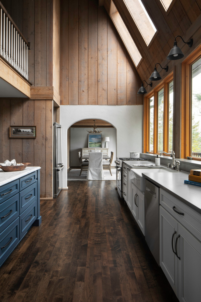 Large country eat-in kitchen in Milwaukee with a farmhouse sink, recessed-panel cabinets, blue cabinets, marble benchtops, metallic splashback, ceramic splashback, stainless steel appliances, medium hardwood floors, with island, brown floor, white benchtop and vaulted.