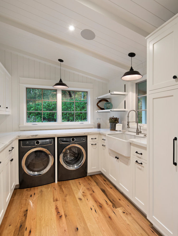 Design ideas for a large country u-shaped dedicated laundry room in San Francisco with a farmhouse sink, shaker cabinets, white cabinets, marble benchtops, white splashback, timber splashback, white walls, light hardwood floors, a side-by-side washer and dryer, white benchtop, vaulted and planked wall panelling.