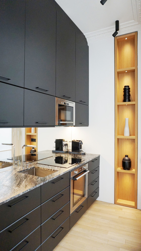 This is an example of a contemporary kitchen in Paris with an undermount sink, flat-panel cabinets, black cabinets, mirror splashback, stainless steel appliances, light hardwood floors, beige floor and grey benchtop.