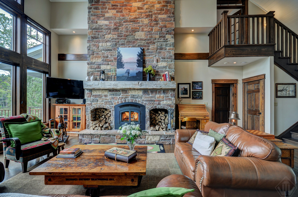 This is an example of a country open concept family room in Other with beige walls, a standard fireplace, a stone fireplace surround and a corner tv.