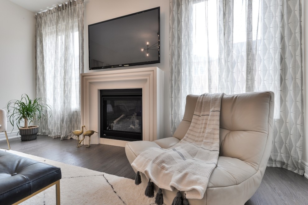 Photo of a large transitional formal open concept living room in Toronto with beige walls, medium hardwood floors, a standard fireplace, a plaster fireplace surround, a wall-mounted tv and grey floor.