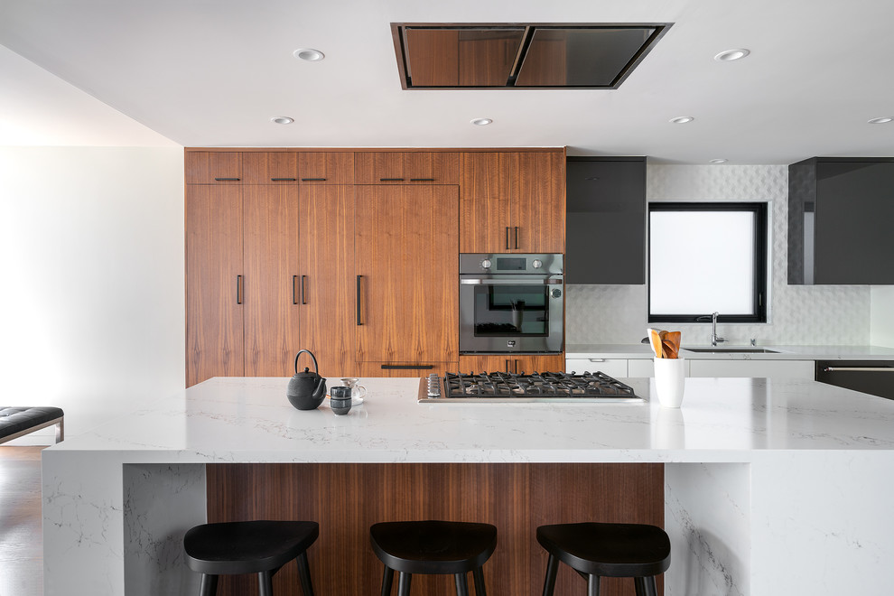 Contemporary galley open plan kitchen in San Francisco with an undermount sink, flat-panel cabinets, dark wood cabinets, white splashback, black appliances, with island and white benchtop.